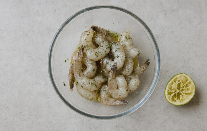Bacon-Wrapped Lime Shrimp, step 2: shrimp marinating in a bowl with lime juice, thyme and olive oil