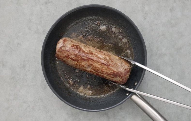 Beef Wellington, step 2: the tenderloin searing in a skillet with oil and butter