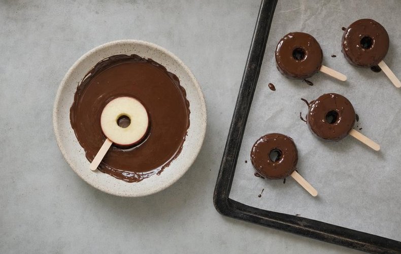 Chocolate Caramel Apples, step 3: apple slices dipped in chocolate on a lined tray