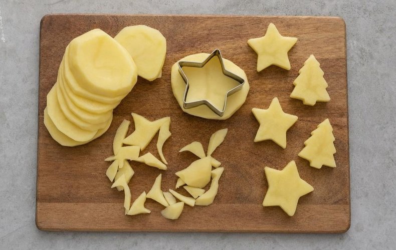 Cutting potato slices into stars and trees with cookie cutters