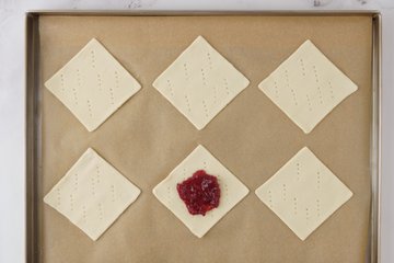 Spooning jam onto the center of the pastry diamonds