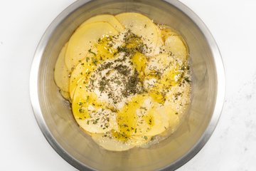 Seasoning the potato slices with cheese, herbs, salt and olive oil