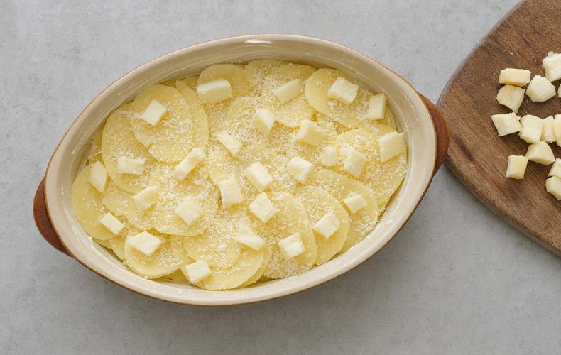 Four Cheese Potatoes, step 2: layering potatoes and diced cheeses in a buttered baking dish
