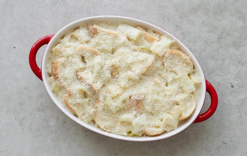 Leek Gratin, step 4: leeks, country bread and béchamel in a baking dish sprinkled with grated Grana