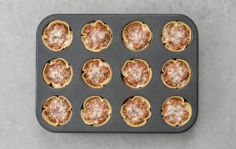 Mini Lasagna Cupcakes, step 6: pasta shells in a muffin pan filled with béchamel, ragù and Parmigiano
