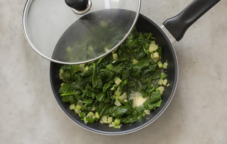 Oysters Rockefeller, step 1: spinach wilting in a skillet with butter and celery