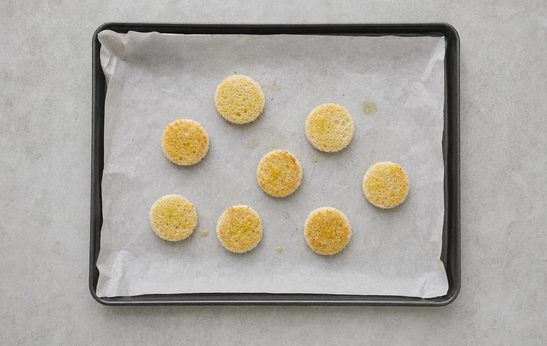 Bread circles drizzled with olive oil on a lined baking sheet
