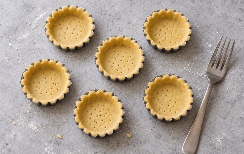 Pastry disks pressed into tartlet molds and pricked with a fork