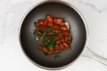 Spaghetti with Clams and Cherry Tomatoes, preparation 6: halved cherry tomatoes with garlic and parsley in a pan