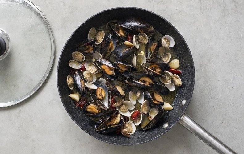 Mussels and clams opening in a covered skillet with garlic and chile