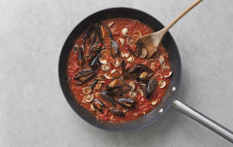 Mussels and clams added to the tomato sauce in a skillet